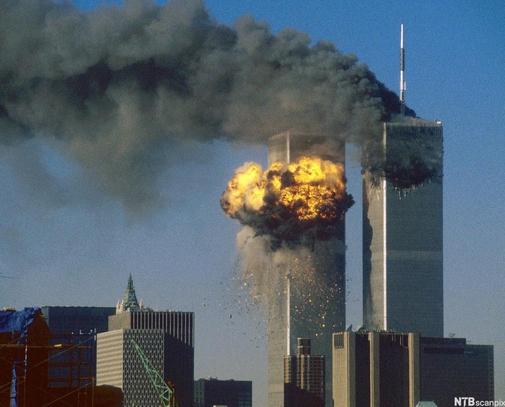 Eksplosjon i det ene tårnet i World Trade Center, som nettopp er truffet av det andre flyet. Fra det andre tårnet, som ble truffet først, stiger tjukk, svart røyk. Foto.