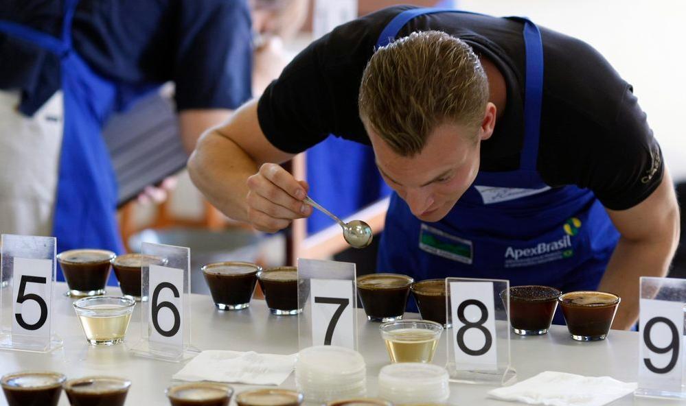En mann står ved et bord og bedømmer ulike sorter kaffe som er nummerert. Foto.