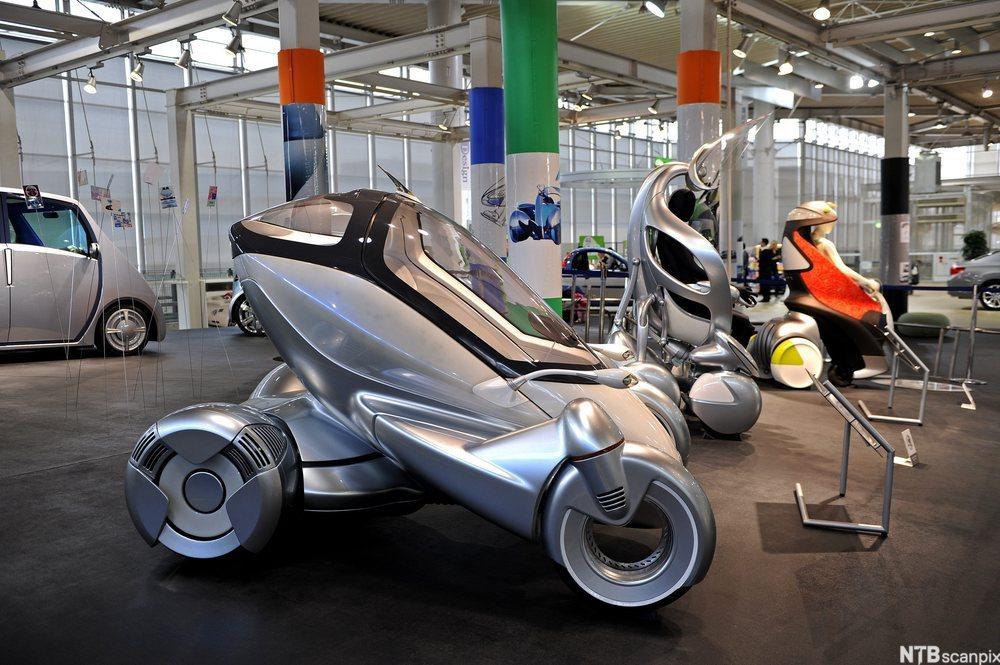 Ulike framtidsrettede framkomstmidler og biler utstilt i en hall. Foto. 