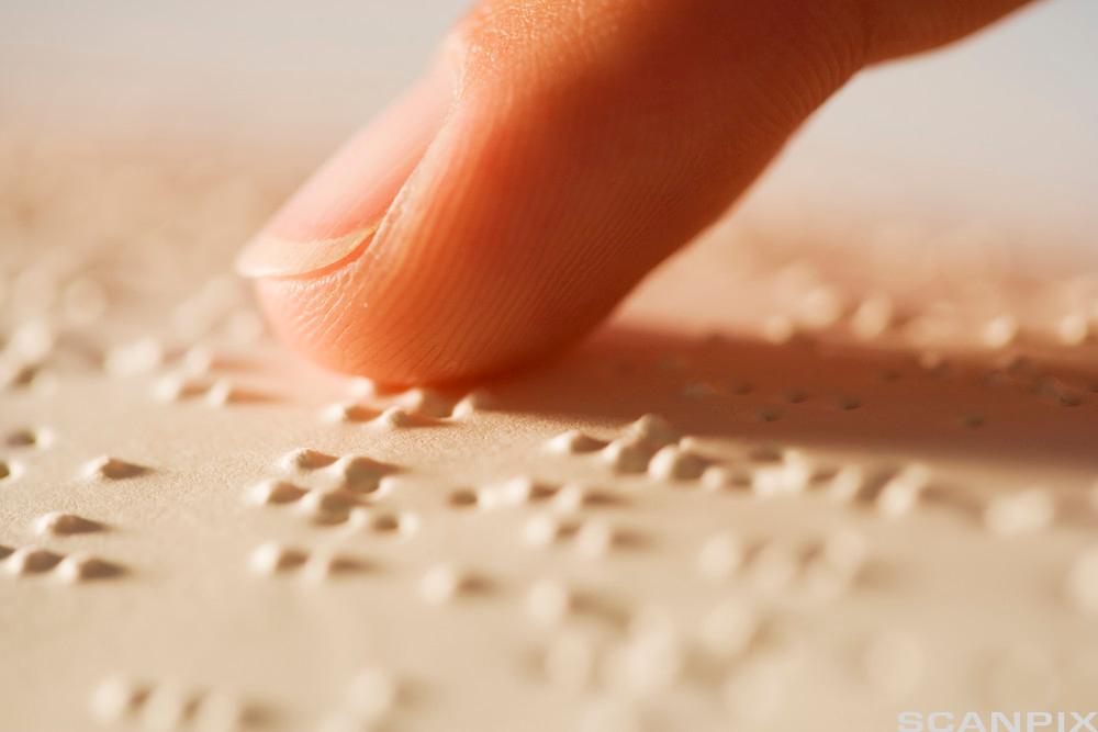 Finger berører små punkter på papiroverflate. Foto.