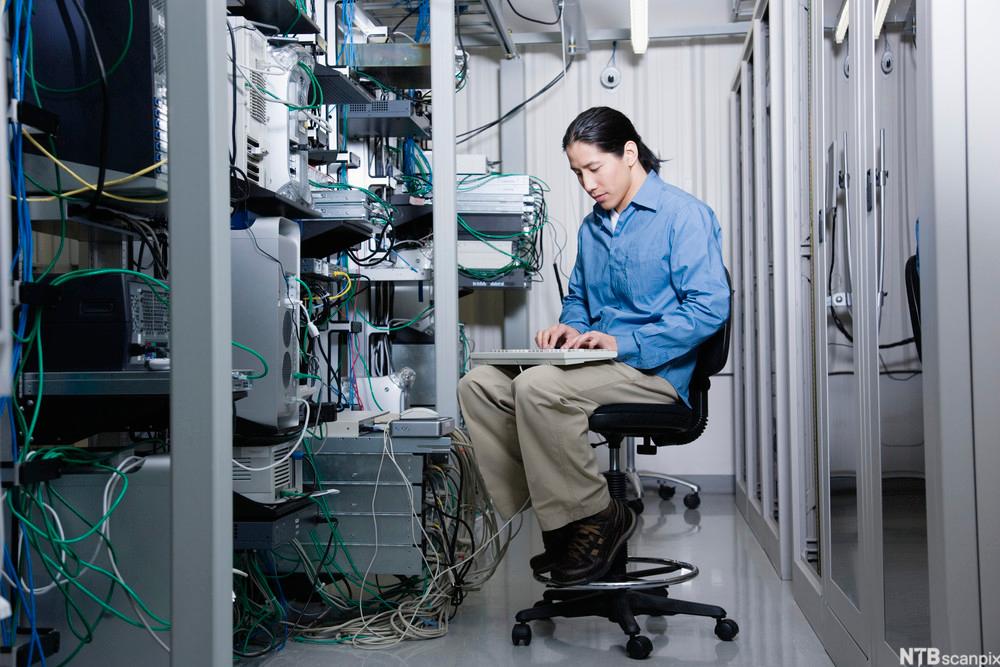 Mann sitter og jobber ved serverrack. Foto