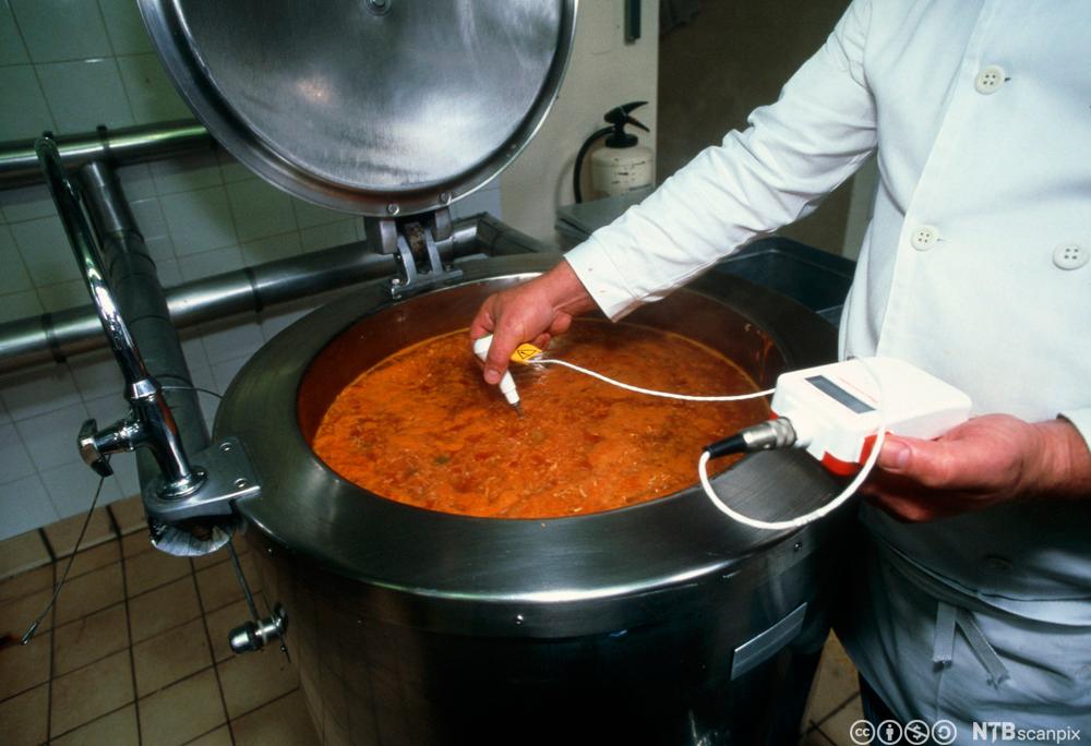 Ein kokk måler temperaturen i ein steamkjele med suppe. Foto.