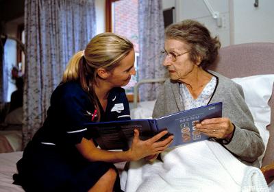 Bilde av en eldre kvinne som får hjelp av en sykepleier til å lese i en sykehus meny