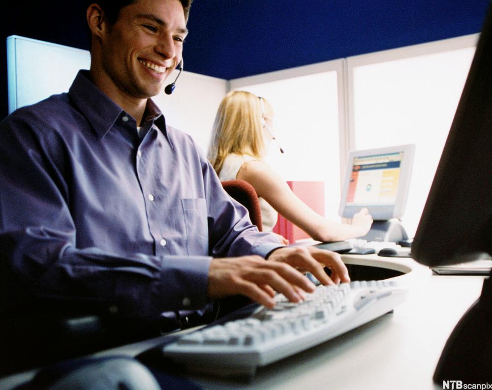Kundeservicemedarbeider som sitter ved datamaskin. Foto.