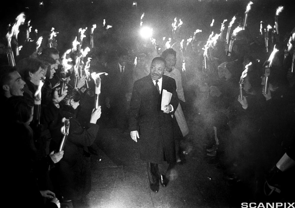 We see Nobel Peace Prize winner Martin Luher King Jr. passing through a crowd of people holding candles and torches in his honour. The photo was taken on Universitetsplassen (University Square) in Oslo in 1964. Photo.