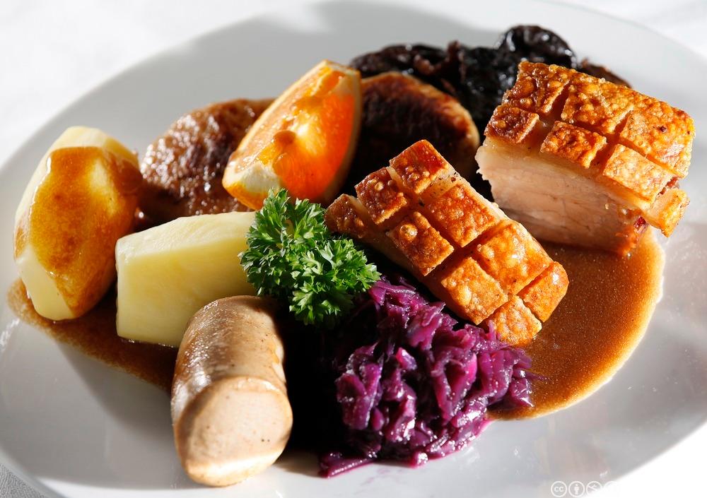 Ein tallerken med ribbe, potet, raudkål, medisterpølse og brun saus. Foto.