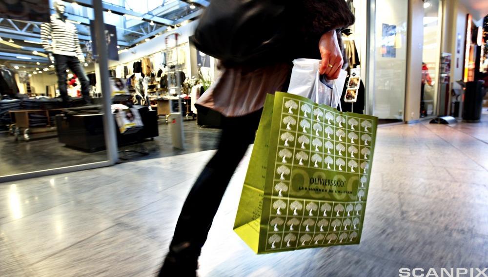 Kvinne som har en papirpose i hånda mens hun går inne i et kjøpesenter. Foto.