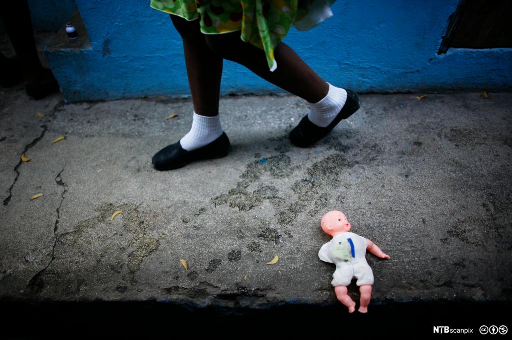 Et barn går forbi en slitt dukke som ligger på fortauet utenfor et barnehjem i Port-au-Prince på Haiti. Foto.