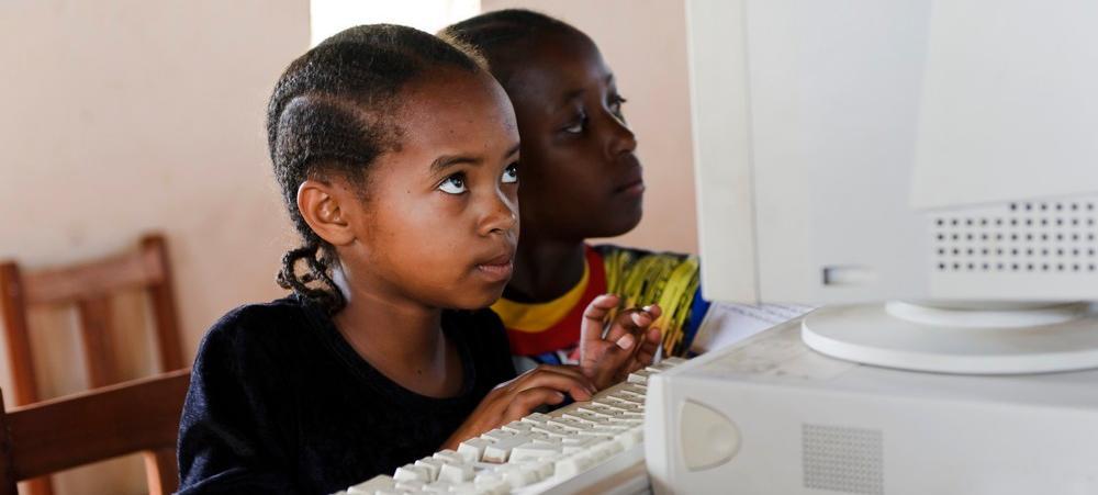 To afrikanske barn sit framom ei datamaskin. Foto.