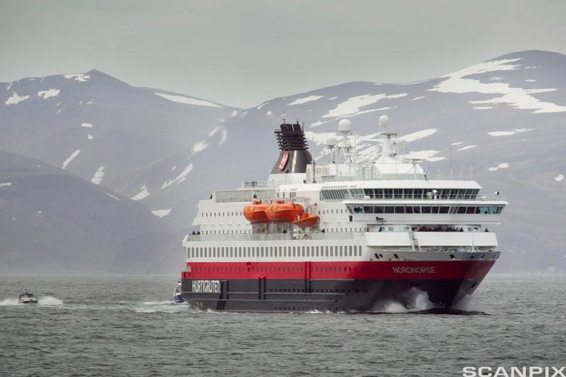Hurtigruteskipet Nord-Norge underveis langs norskekysten. I bakgrunnen er det åser og fjell som er delvis dekt med snø. Foto.