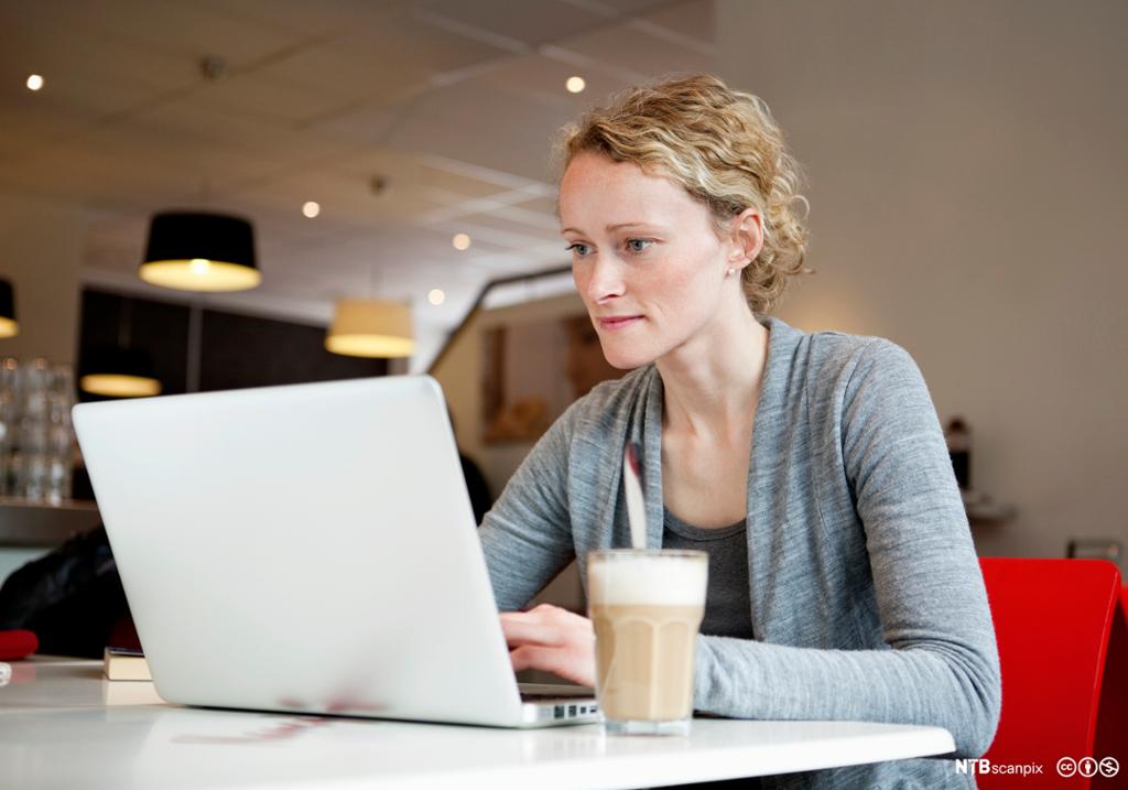 Kvinne sitter på en kafe med laptop. Foto.