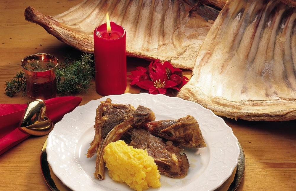 Pinnekjøttallerken med kålrotstappe anrettet på hvit tallerken. Det står et rødt kubbelys og andre juledekorasjoner på bordet. Foto.