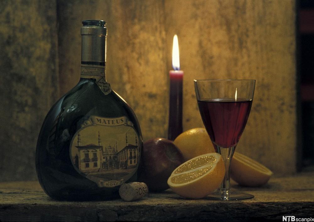 Flaske med rosévin, vinglas, stearinlys og frukt i ein vinkjellar. Foto.