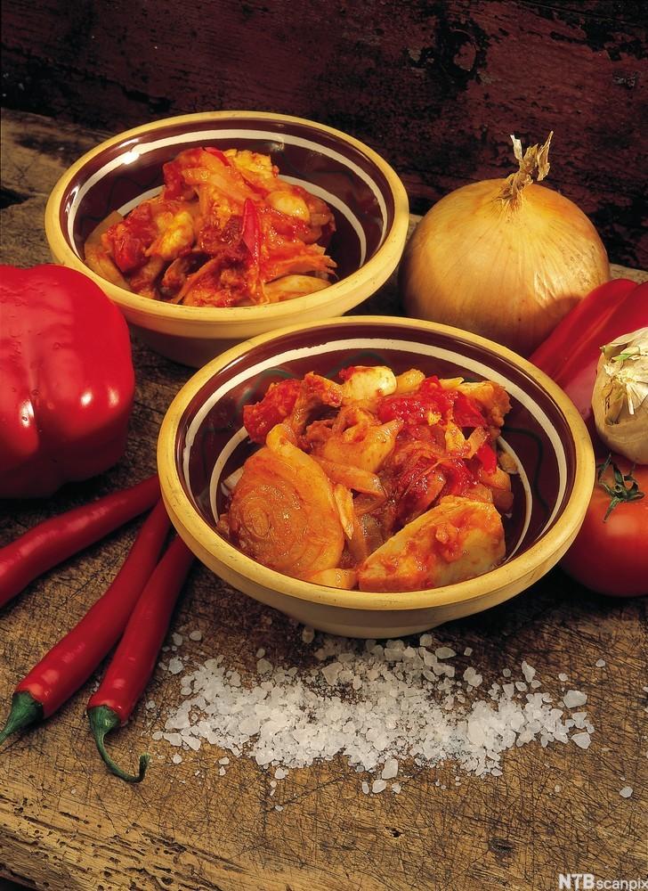 To porsjonar bakalao i skåler på eit trebord, med raud chili, lauk, paprika, tomat, kvitlauk og salt ved sida av. Foto.