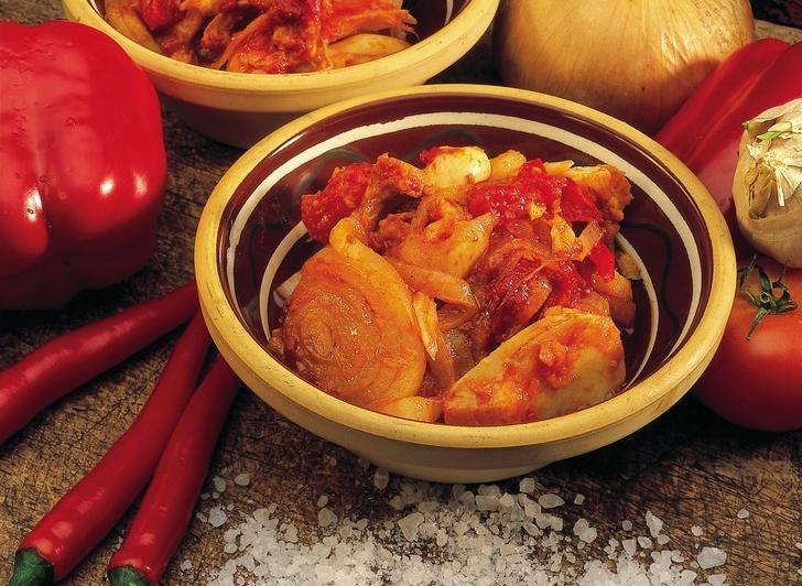 En porsjon bacalao i en skål. Noen hele grønnsaker, blant annet paprika, løk og chili, ligger ved siden av. Foto.