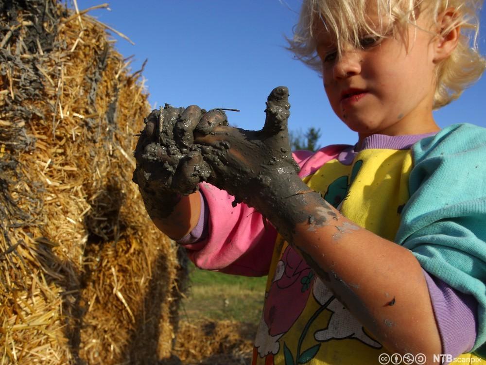 Eit barn gnir hendene som er fulle av gjørme. Foto.