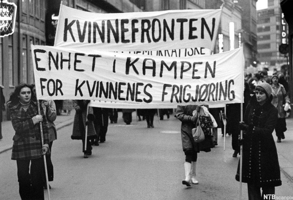 Kvinner går i 8. marstog 1973. Fremst er to kvinner som held kvar sin ende av eit banner med teksten "Enhet i kampen for kvinnenes frigjøring". Foto.