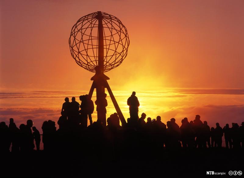 Turister i solnedgang på Nordkapp. Motlys. Foto.