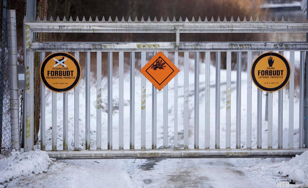 En elektrisk drevet port med tagger på toppen stenger en snødekket vei. På porten henger flere gule og oransje forbudsskilt. Foto.