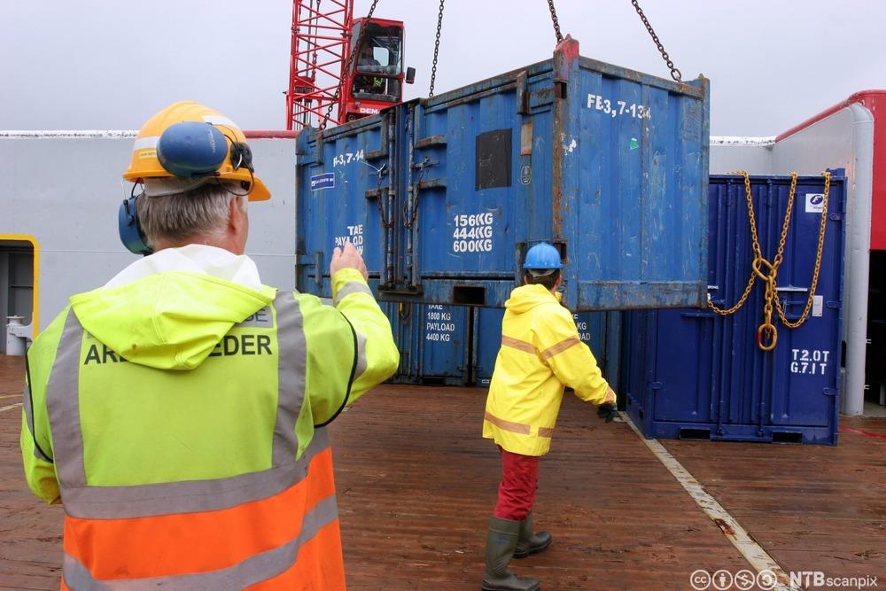 To flaggfolk sørgjer for at konteinarar blir landa om bord på ein supplybåt. Foto.