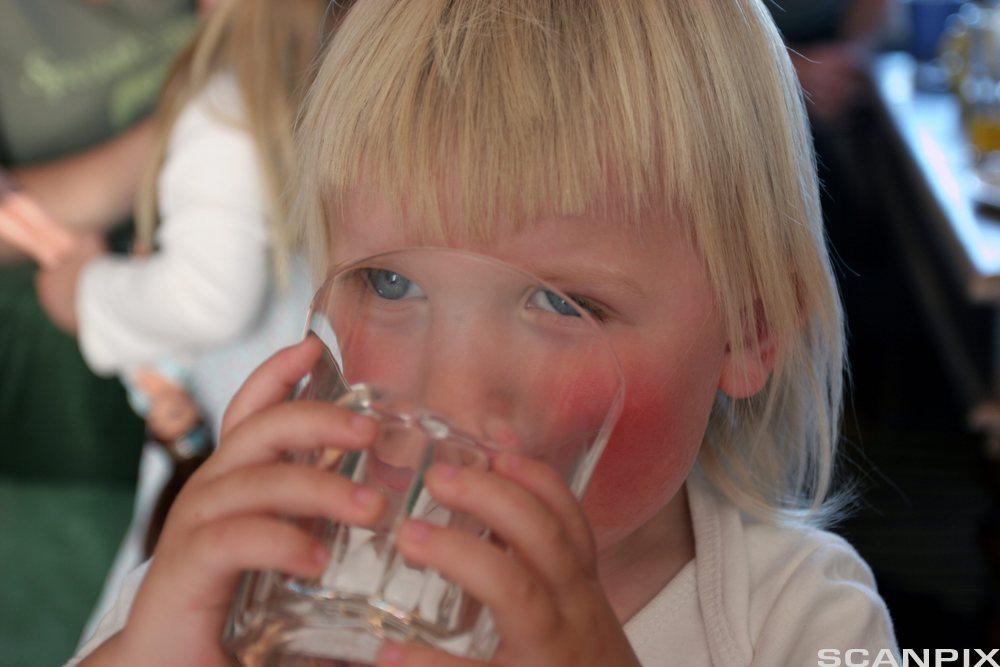 Ein liten gut drikk frå eit vassglas. Foto.