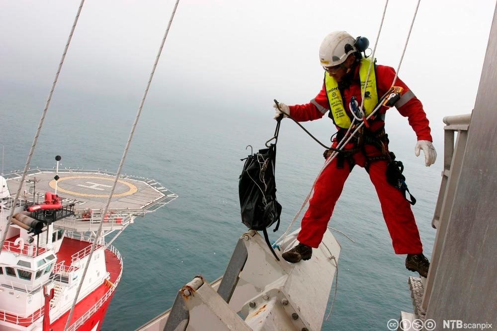 En klatrer i arbeid på en oljeplattform i Nordsjøen. Nede på havet ligger en supplybåt og venter. Foto.