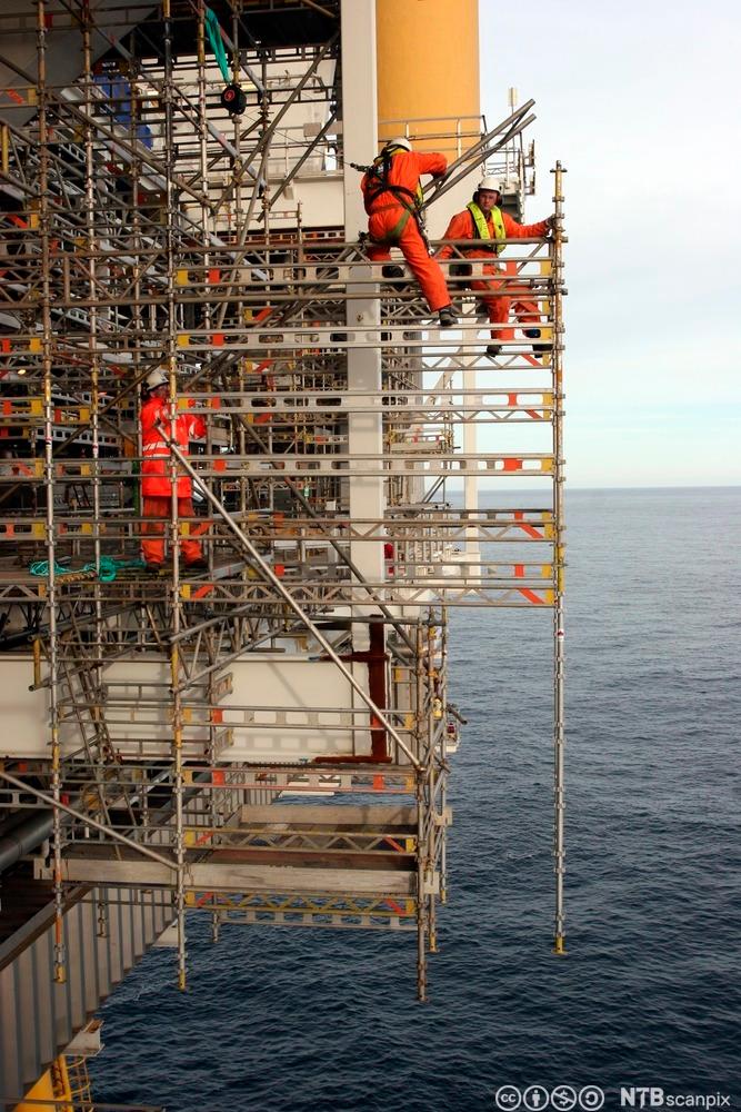 To arbeidere som er sikret med seler, monterer et stillas på en oljeplattform. Under dem er det fritt fall ned i havet. Foto.