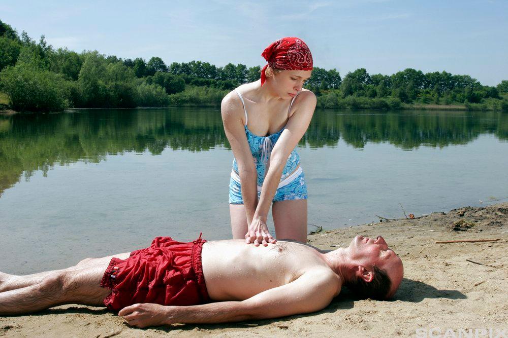 Dame utfører HLR på en mann på stranda. Illustrasjonsfoto.