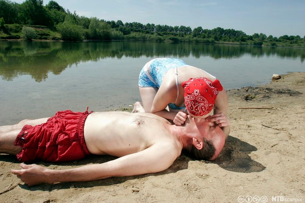 En ung kvinne hjelper en mann som er bevisstløs på stranden ved å gi munn til munn. Foto.