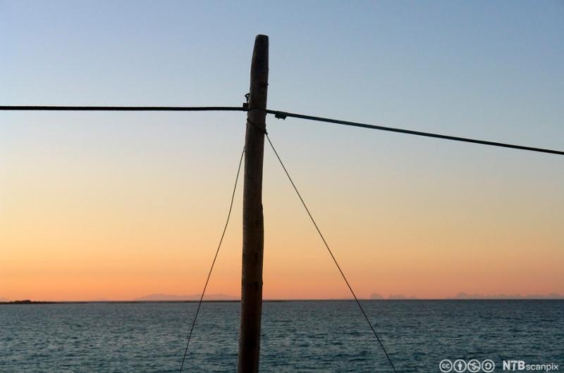Telefonstolpe med solnedgang over sjøen som bakgrunn. Foto.