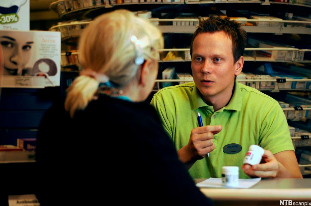 Ein mannleg seljar i grøn t-skjorte snakkar med ei kvinne som har ryggen til. Foto.