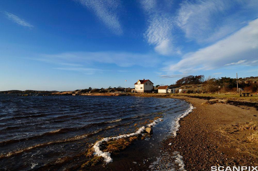 Landskap med blå himmel, mark og et hus i det fjerne. Foto.