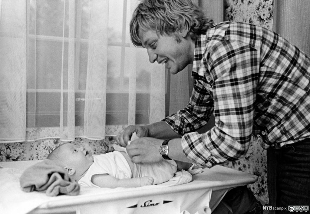 En far som prater med et lite barn som ligger på stellebordet. Foto.