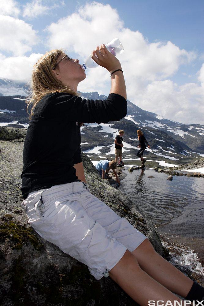 Jente som drikker vann fra flaske på fjelltur. Foto.
