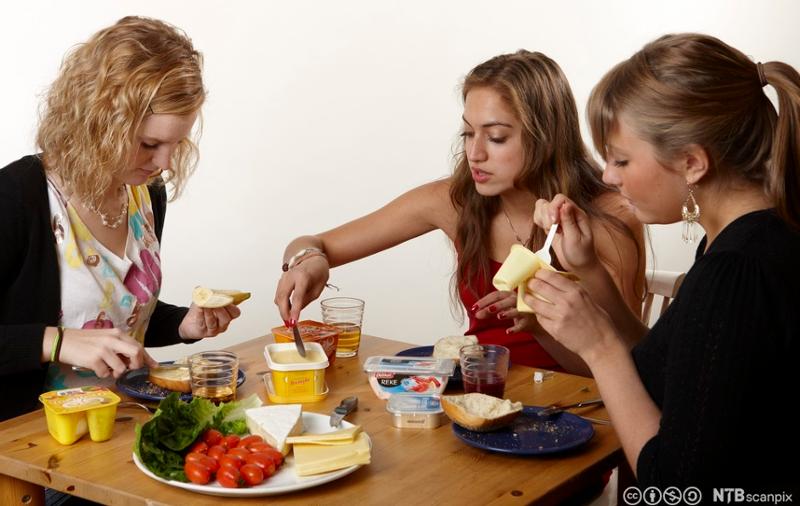 Tre unge jenter sitter rundt et bord og spiser frokost. Foto.
