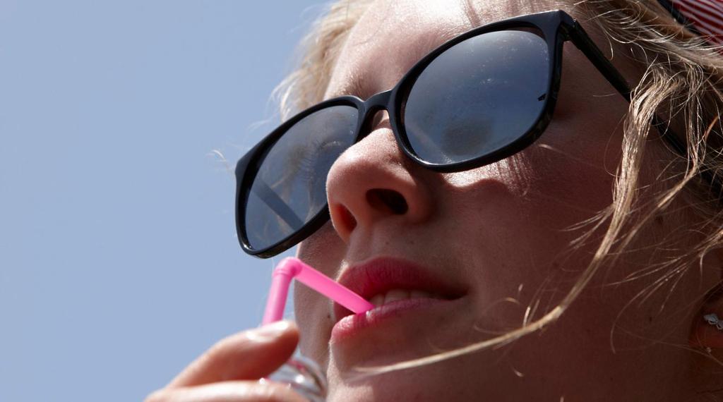 Jente med solbriller drikker leskedrikk med sugerør. Foto.
