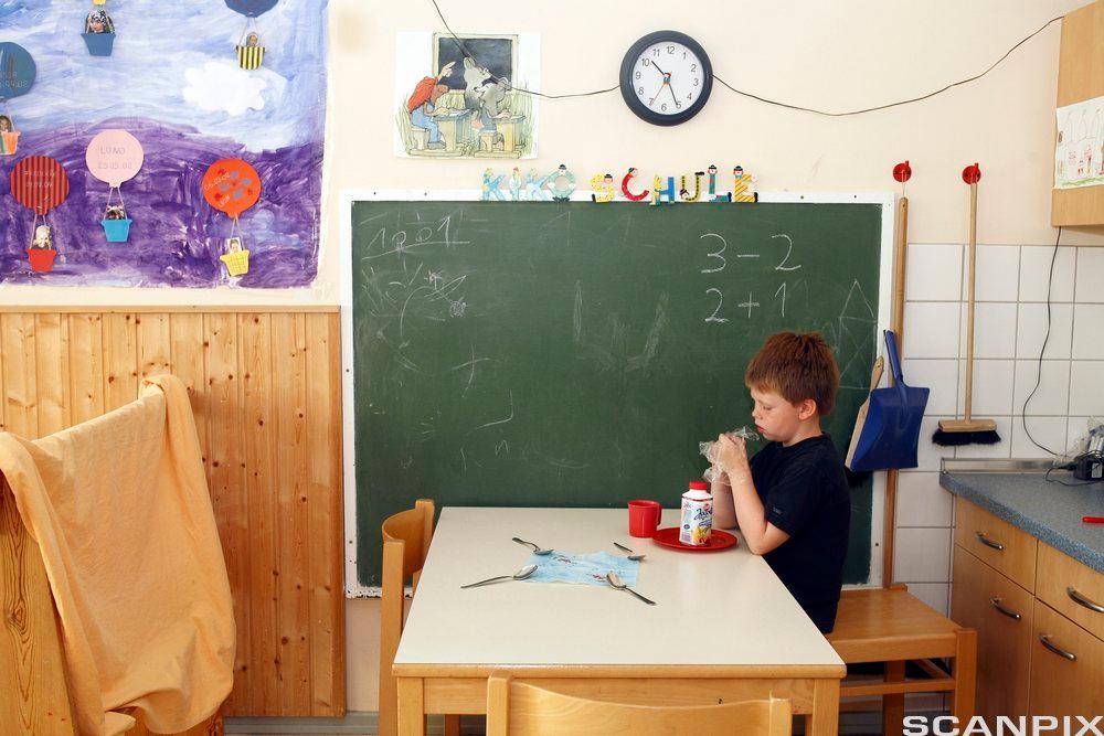 Eit barn sit ved eit bord i eit klasserom. Foto. 