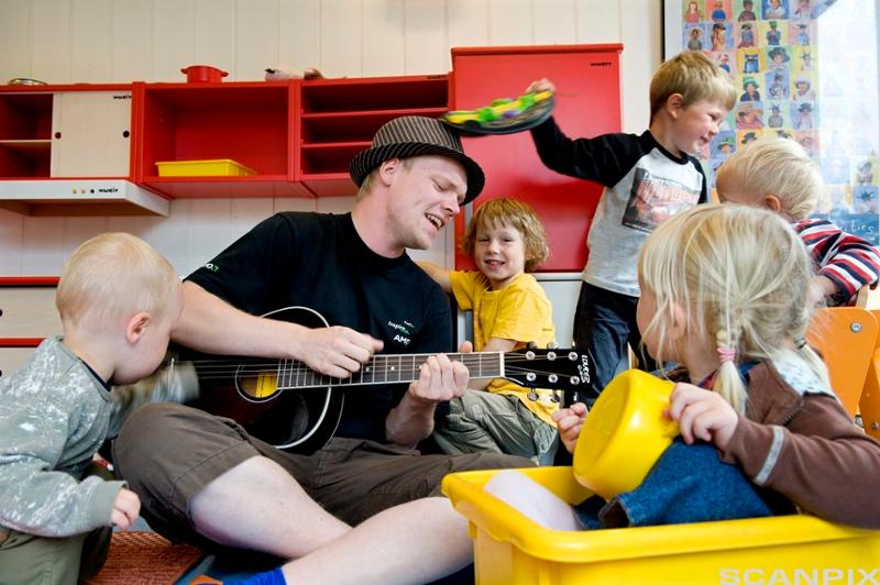 Barnehageansatt spiller synger med barna. Foto.