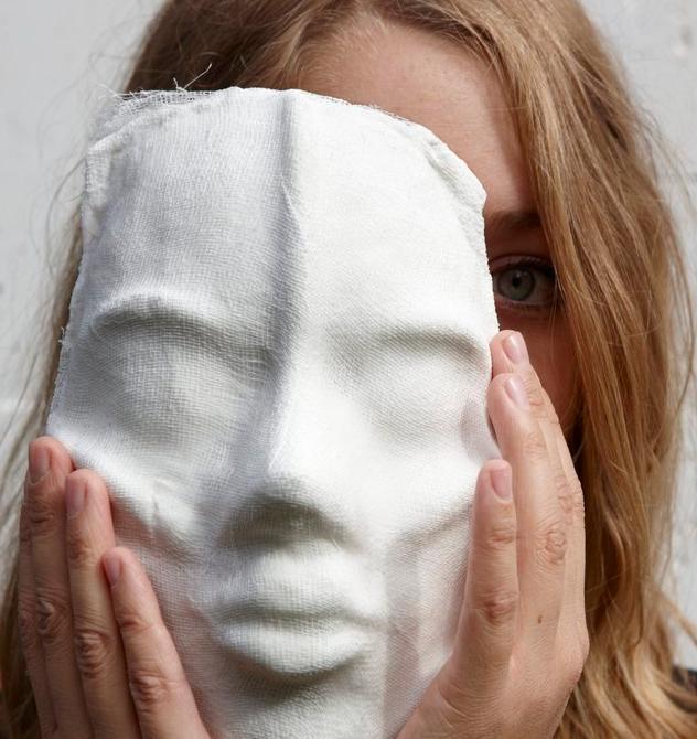 Jente som holder en maske delvis foran ansiktet. Foto.