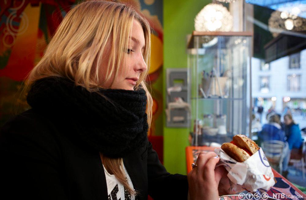 En jente på kafe holder noe brødmat i hånden. Foto.