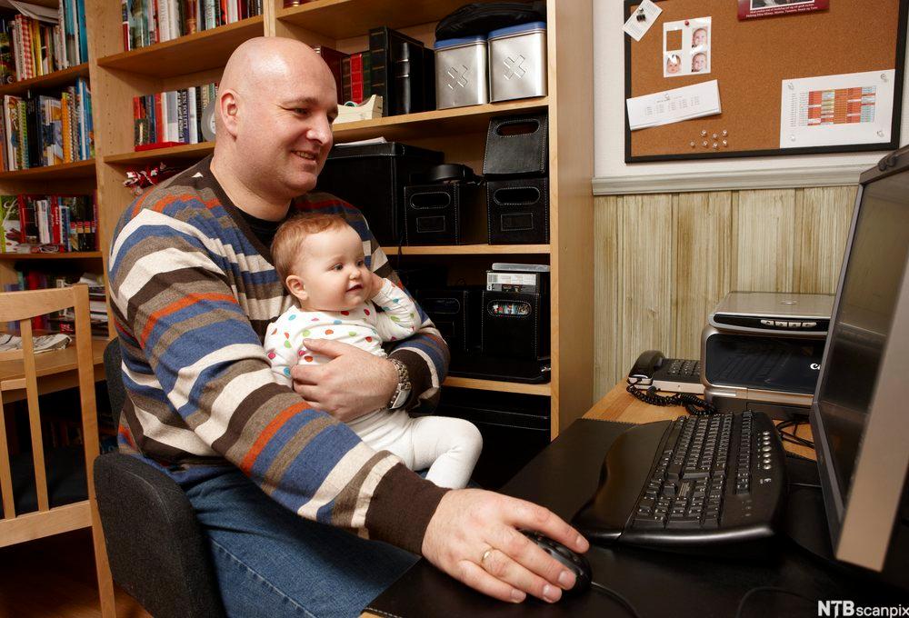 Mann sitter med lite barn i fanget mens han arbeider på PC hjemmefra. Foto