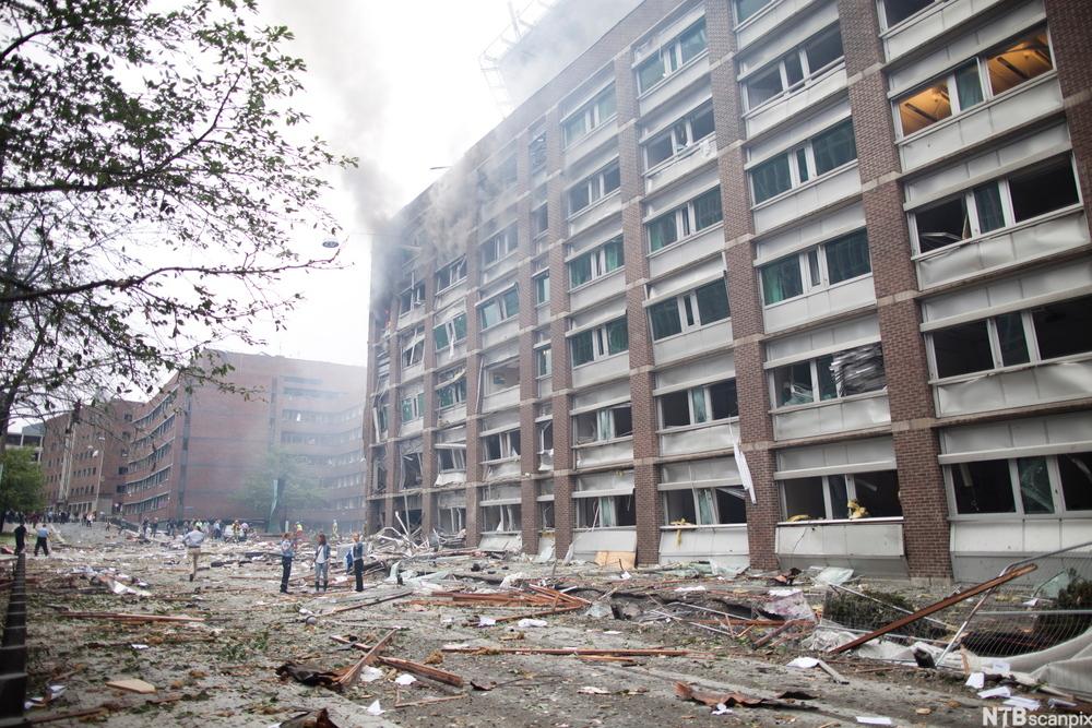 Bygning i Regjeringskvartalet etter terrorbomben. Alle vinduene er knust, og bygningsdeler er spredd utover plassen foran bygningen. Foto.