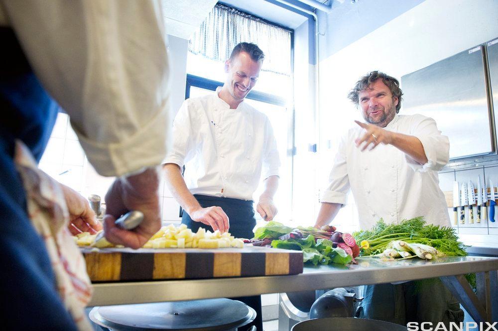 To kokker smiler og har det hyggelig sammen mens de jobber på restaurantkjøkken. Foto.