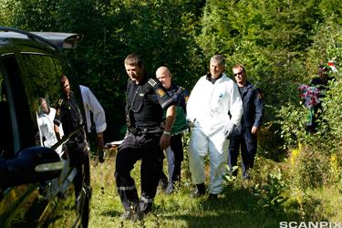 Politifolk i uniform og hvit overtrekksdress bærer bort en omkommet person. Foto.