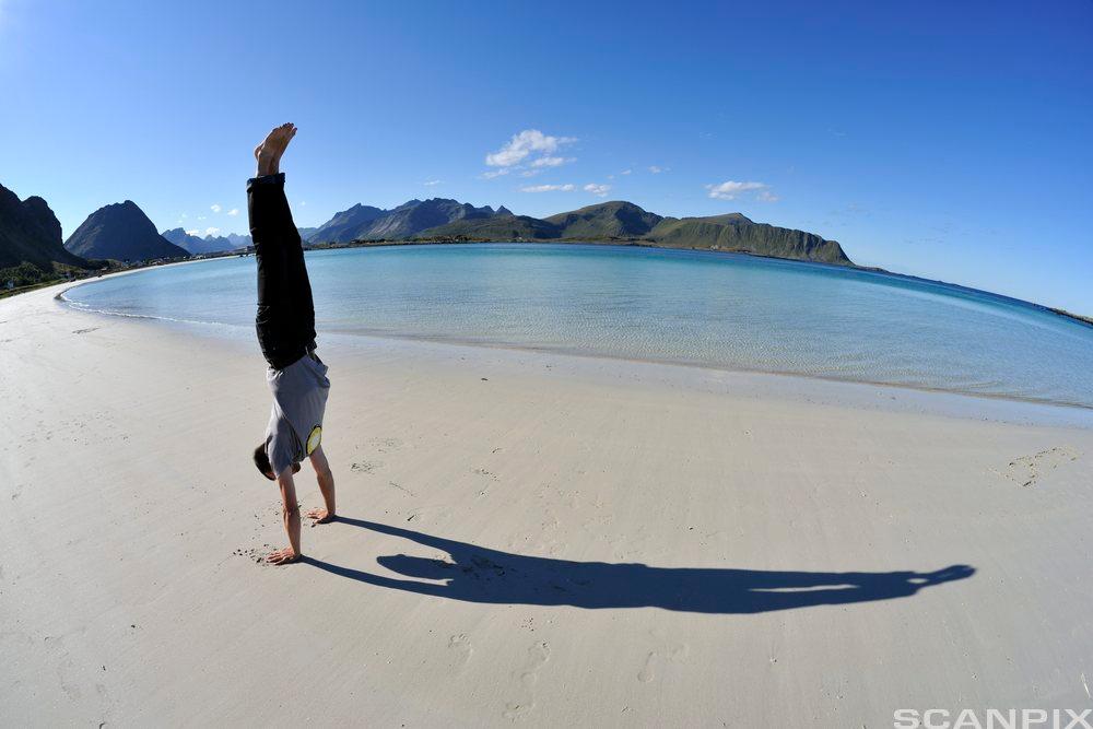 Person som står på hendene på en strand med horisonten bak. Foto.