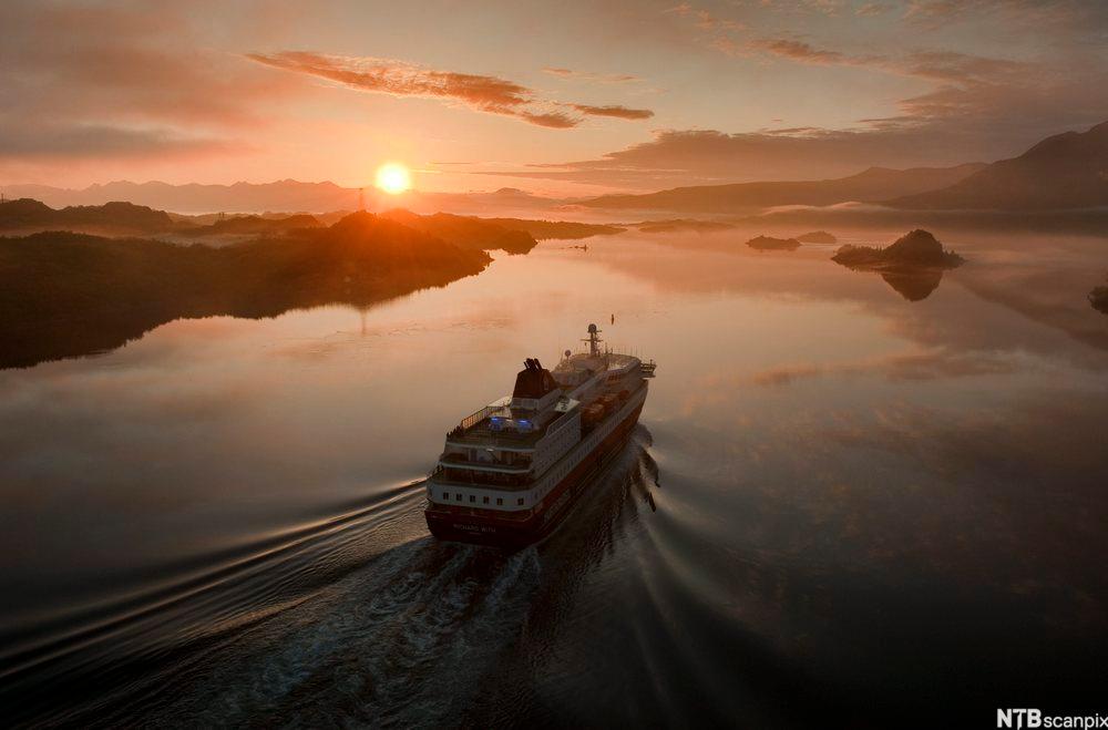 Ei norsk ferje på blikstilt vatn med ein solnedgang framfor seg. Foto.