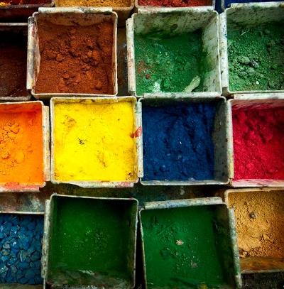 Åpne bokser fylt med forskjellige fargerike pigmenter. Hver boks er fylt med hver sin farge, inkludert rød, oransje, gul, grønn, blå og brun. Foto.