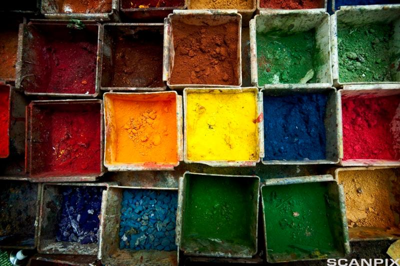 Åpne bokser fylt med forskjellige fargerike pigmenter. Hver boks er fylt med en annen farge, inkludert rød, oransje, gul, grønn, blå og brun. Foto.