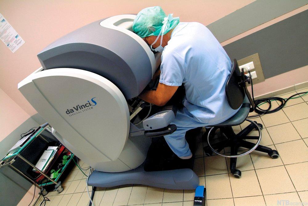 Kirurg sitter ved en konsoll og operer via fjernstyring. Foto.
