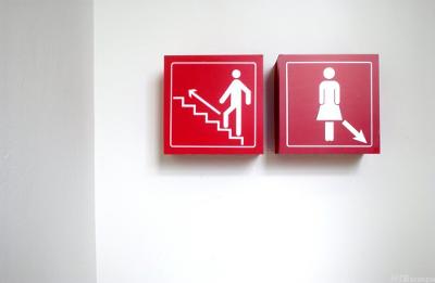 Piktogram med mann som går opp en trapp og et skilt med en kvinne og en pil som peker nedover. Foto. 